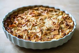 Une tarte aux pommes dorée et croustillante, présentée dans un moule à tarte blanc, avec des tranches de pommes disposées en surface, illustrant un dessert classique et gourmand de la gastronomie corrézienne. 