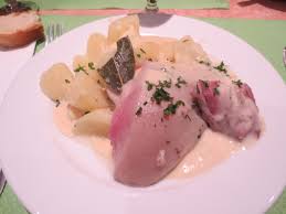 Un plat traditionnel français de tête de veau servi avec une sauce onctueuse et des pommes de terre, présenté dans une assiette blanche, illustrant une spécialité culinaire rustique et authentique à la gastronomiee corrézienne.